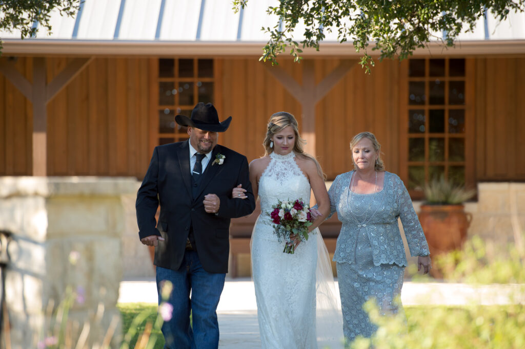 bride getting escorted during processional by both her parents