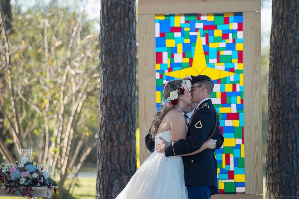 bride and groom sharing the first kiss in front of a replica of a stained glass church window at strawberry pines wedding venue by San Antonio TX Wedding Photographer Tammy Blalock, Ata-Girl Photography Co.