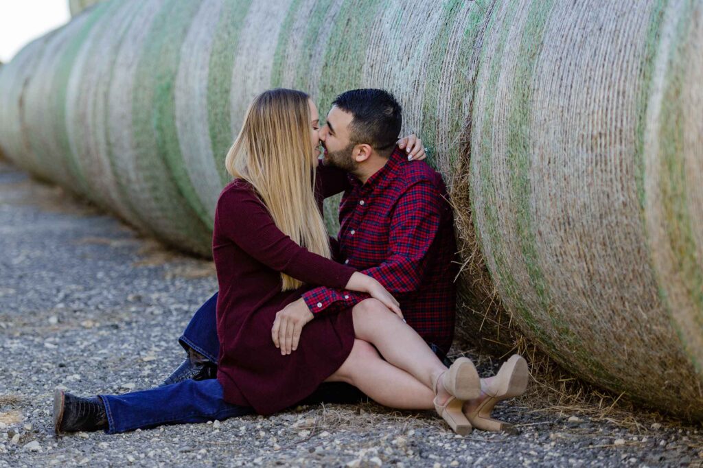 couple kissing beside a round bale of hay during their country engagement session by San Antonio TX Wedding Photographer Tammy Blalock, Ata-Girl Photography Co.