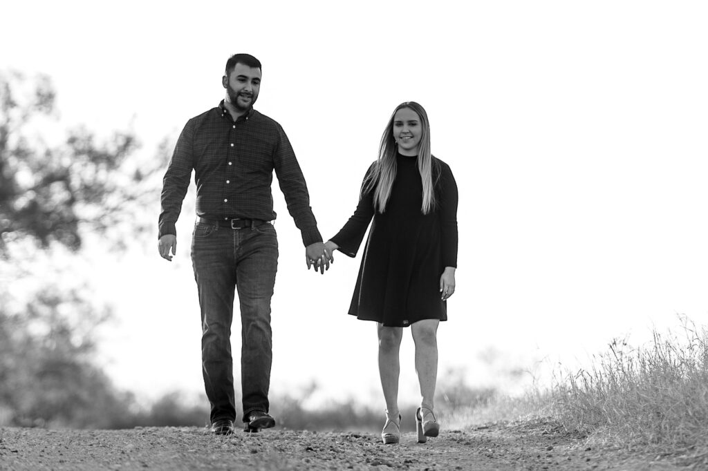 country engagement session black and white image of a couple walking hand in hand down a country road on a ranch by San Antonio TX Wedding Photographer Tammy Blalock, Ata-Girl Photography Co.