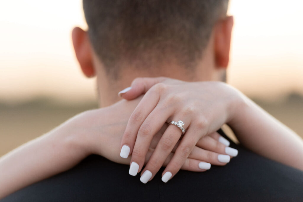 country engagement session close up shot of the engagement ring on the fiance's finger as she's hugging her partner's neck by San Antonio TX Wedding Photographer Tammy Blalock, Ata-Girl Photography Co.