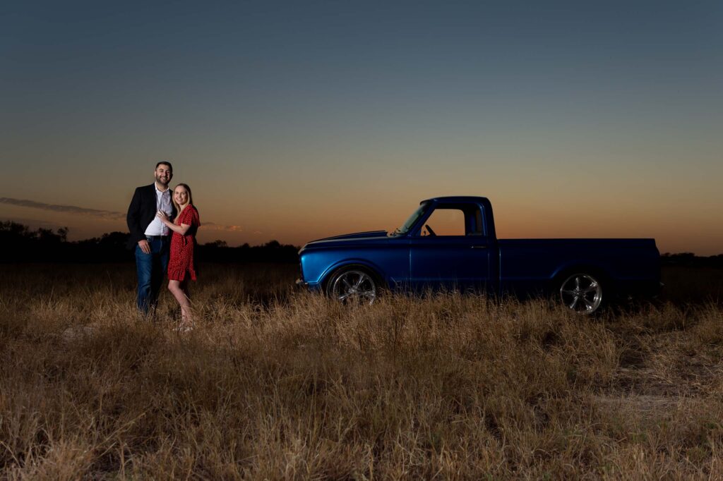 one of the last shots of the night during the country engagement session of the couple standing in front of their classic truck as the sun sets in an open field by San Antonio TX Wedding Photographer Tammy Blalock, Ata-Girl Photography Co.